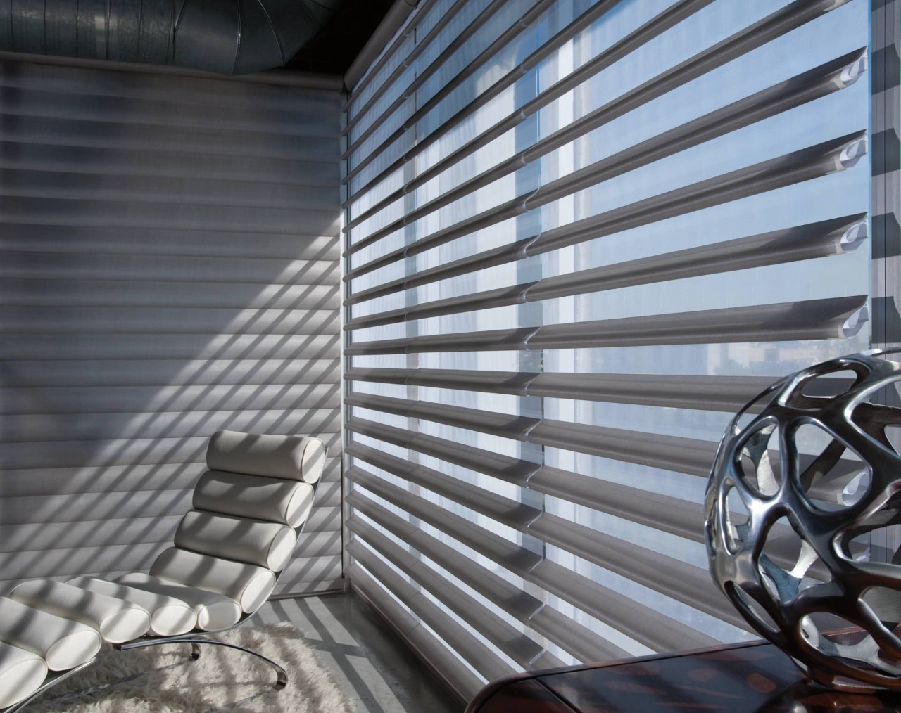 Hunter Douglas Pirouette® Window Shadings casting lined shadows into a room with a white leather chair at WTI Inc near Concord, MA