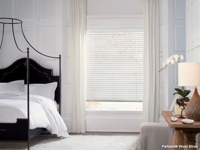 A bedroom with white walls, bedding and window coverings with a black bed.